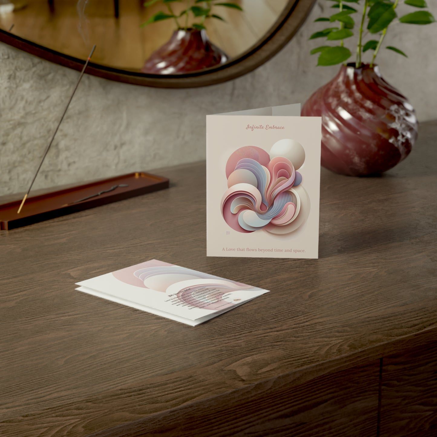 Artistic greeting card and envelope styled on a dark wood table beside a sculptural vase and mirror, offering a warm gifting mood.