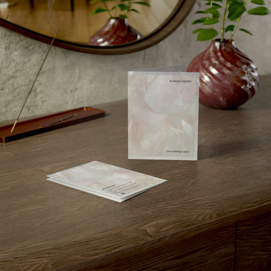 Lifestyle image of the “In Bloom, Together” wedding card standing on a wooden table beside a sculptural vase and incense tray. The card features abstract petals and the message “A love unfolding in grace”, captured in a warm, intimate setting ideal for modern, poetic couples.