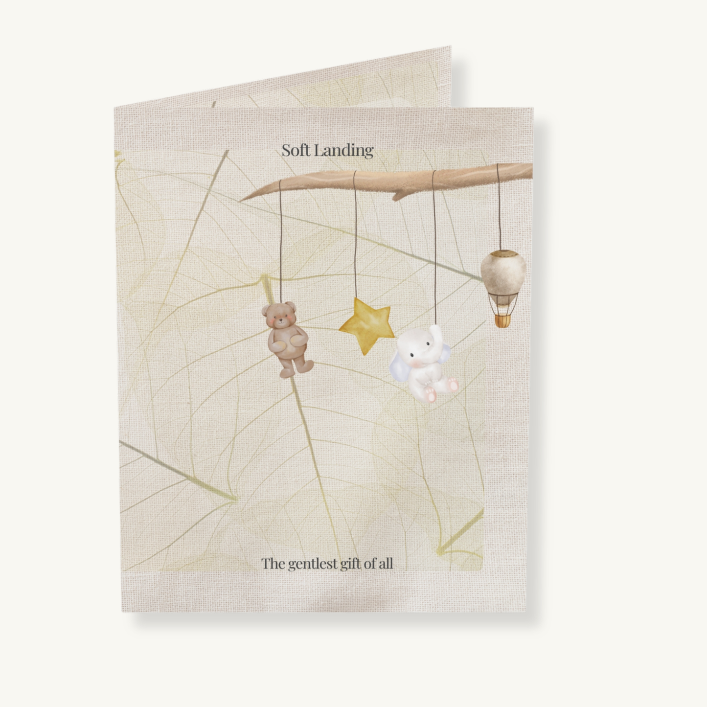 Soft Landing baby greeting card featuring a dreamy mobile with bear, bunny, star, and balloon, set on linen and leaf textures — a gentle welcome gift for new parents.