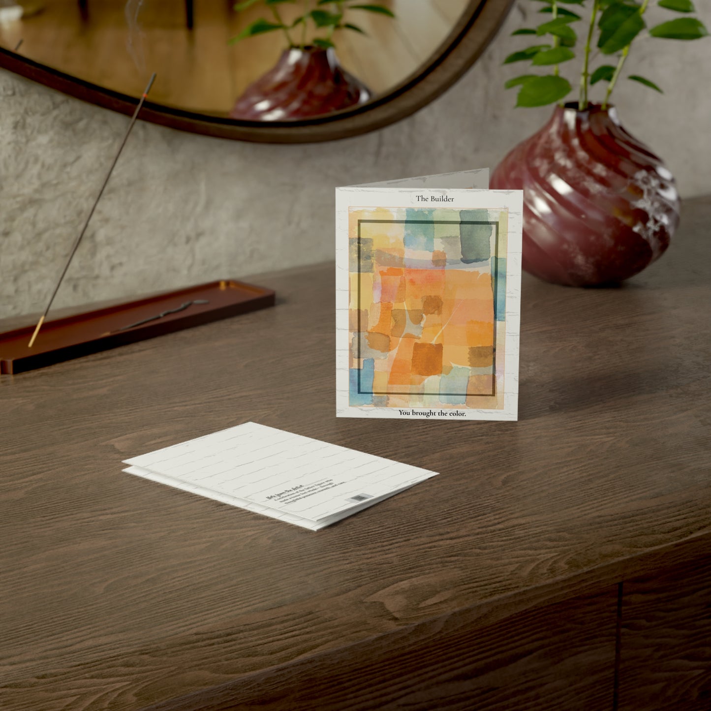 “The Builder” art greeting card styled in a warm lifestyle scene with home decor accents. Featuring an abstract watercolor design in soft orange and golden tones, the card rests on a wooden surface with cozy props, perfect for Father’s Day gifting. A heartfelt card for dads, mentors, or chosen family.