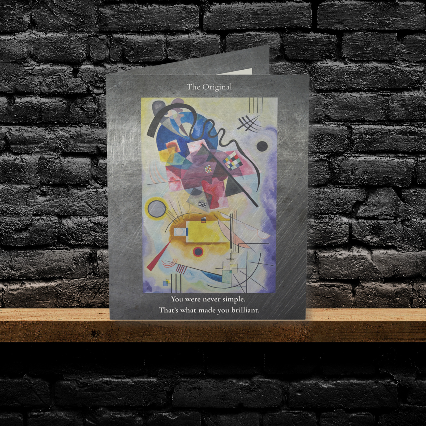 A folded A6 art greeting card titled “The Original,” featuring a bold abstract artwork layered on brushed steel. Displayed upright against a black brick wall, this card is perfect for creative dads and unconventional father figures—designed by Printed Echoes Creations.