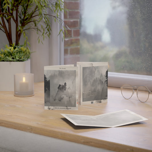 A folded A6 art greeting card titled “The Steady One,” featuring a misty ink-wash mountain landscape in grayscale tones. Displayed upright on a wooden shelf against a black brick wall. A minimalist Father’s Day card for quiet, steady dads, stepdads, or mentors—designed by Printed Echoes Creations.