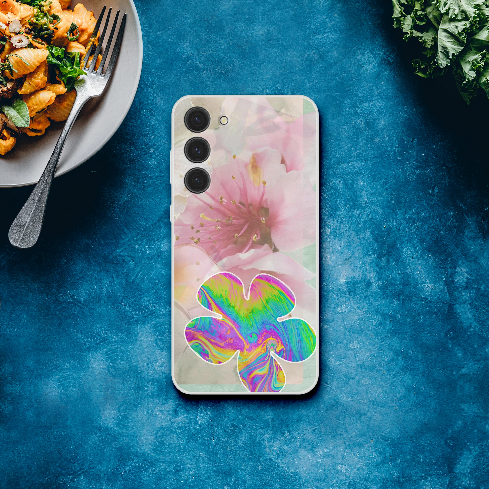 Samsung Galaxy S23 Plus phone case on a bold blue background next to a plate of pasta, featuring cherry blossom florals with a vibrant psychedelic flower – artistic, aesthetic, and slim shockproof case.
