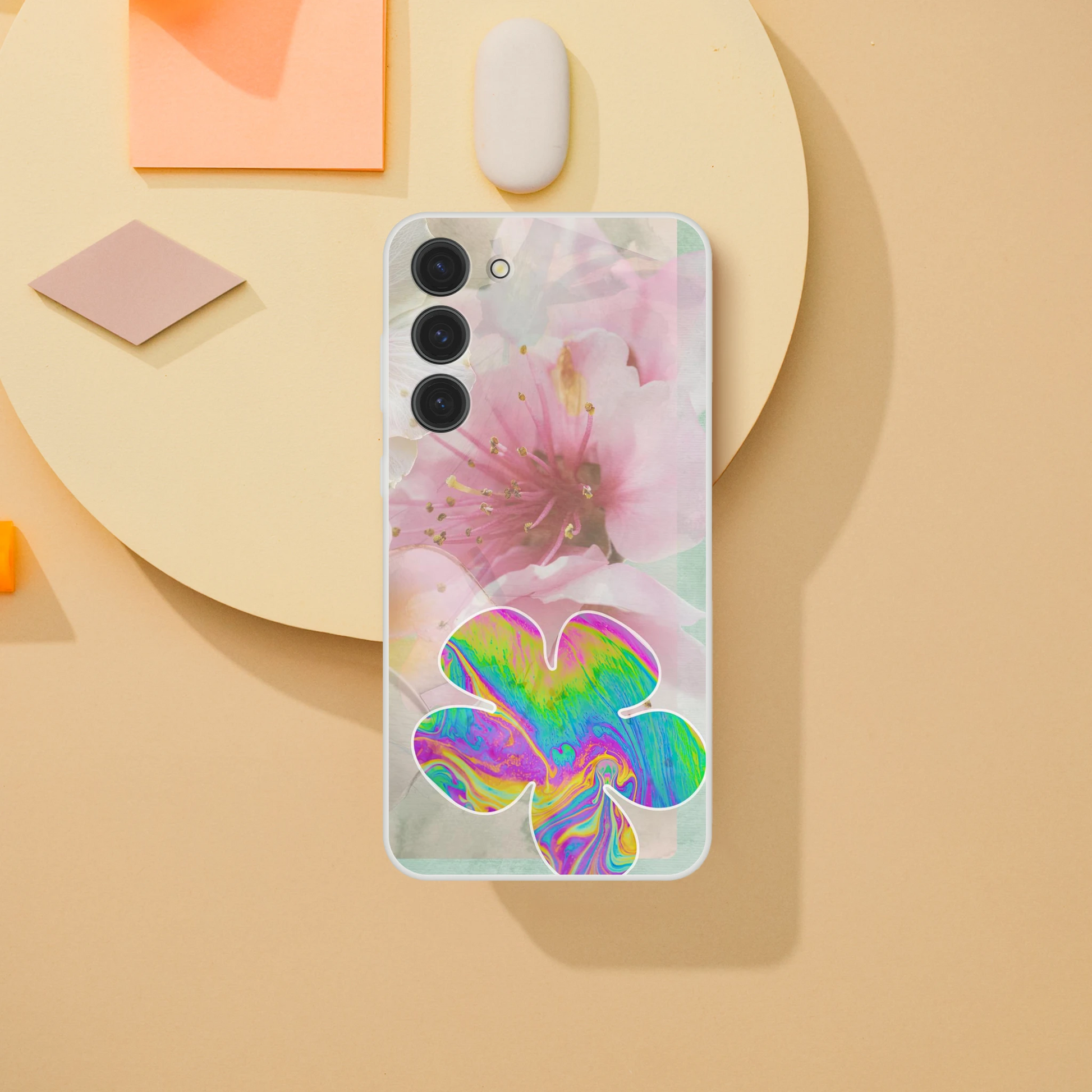 Samsung Galaxy S23 Plus phone case on a soft yellow backdrop with modern minimal objects, featuring pink cherry blossoms and a bold psychedelic flower—artistic and protective design for spring.
