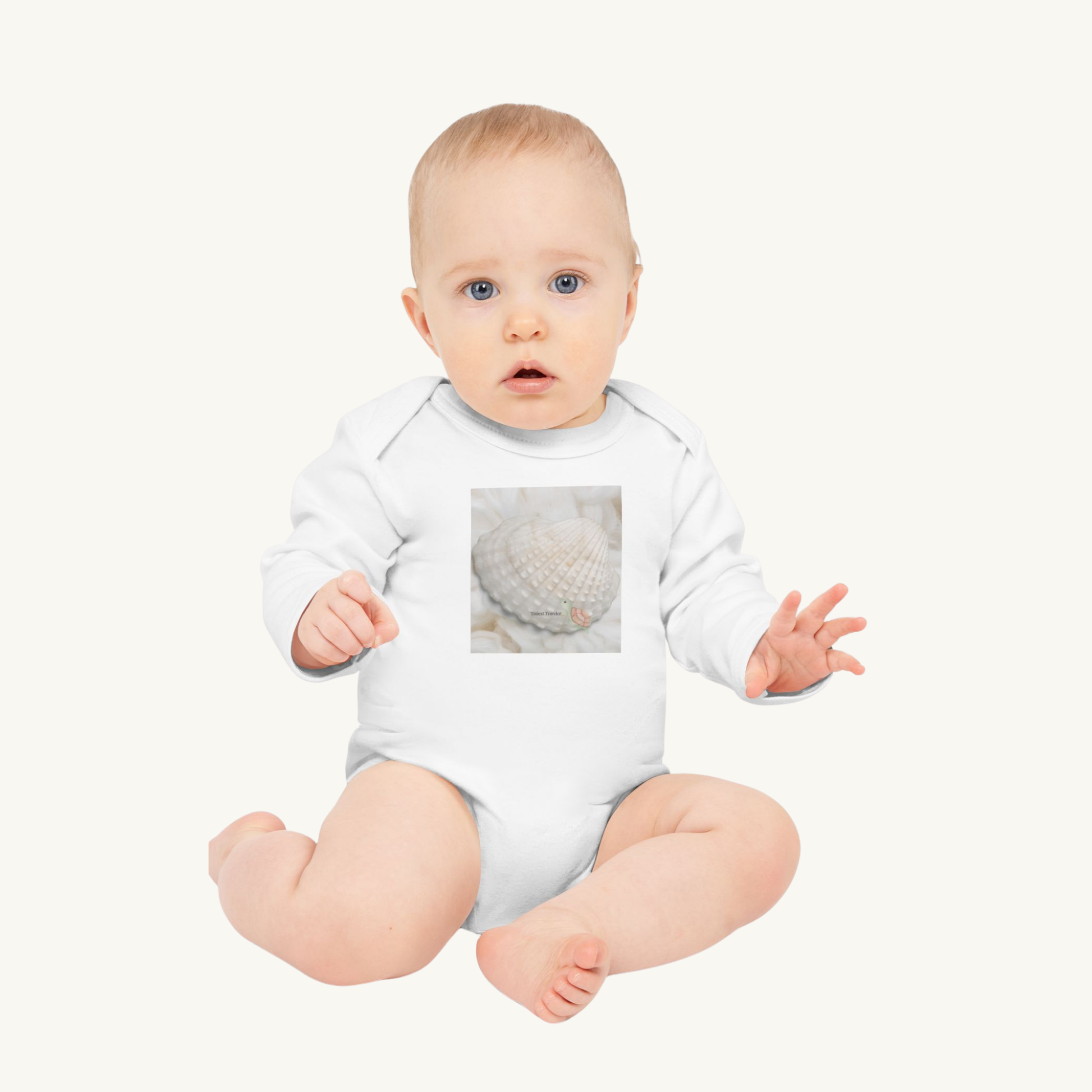 Baby wearing the Tiniest Traveler organic white bodysuit, seated on a blush background. A soft and poetic lifestyle image.