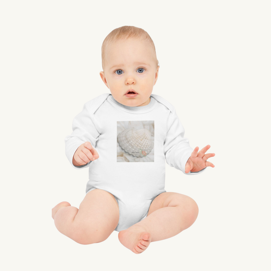 Baby wearing the Tiniest Traveler organic white bodysuit, seated on a blush background. A soft and poetic lifestyle image.