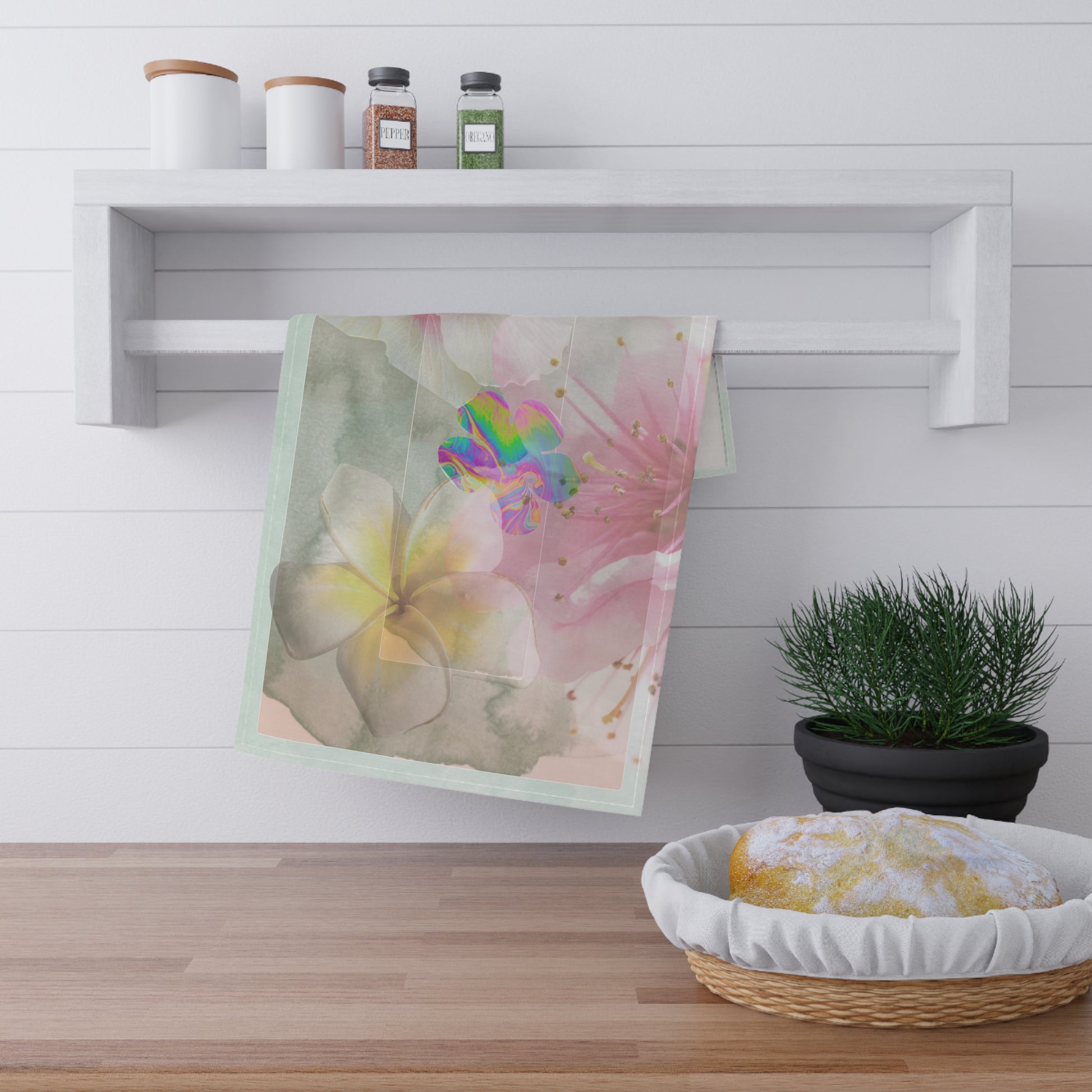 Bloom, Baby, Bloom! tea towel displayed on a white kitchen rack beside fresh bread and herbs, showcasing its artistic floral design in a cozy countertop setting.