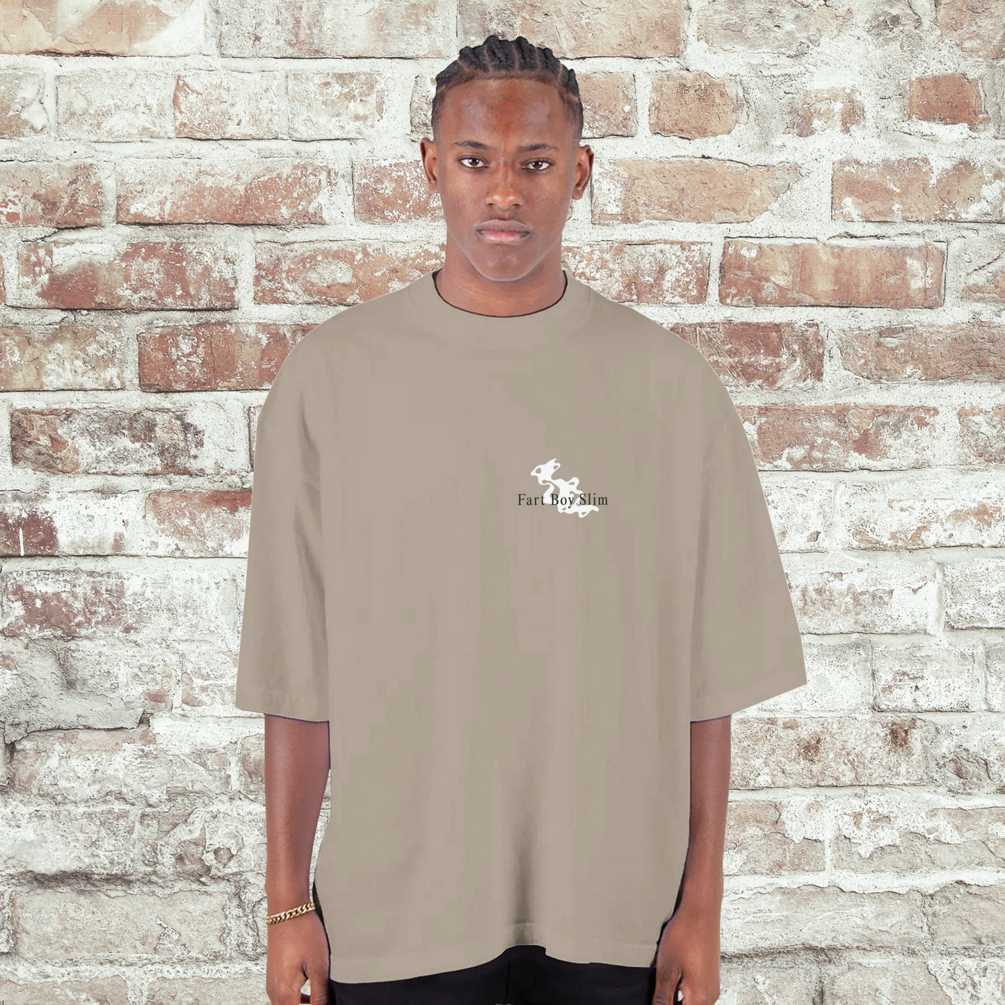 Front view of oatmeal Fart Boy Slim oversized graphic t-shirt worn in front of a white brick wall.