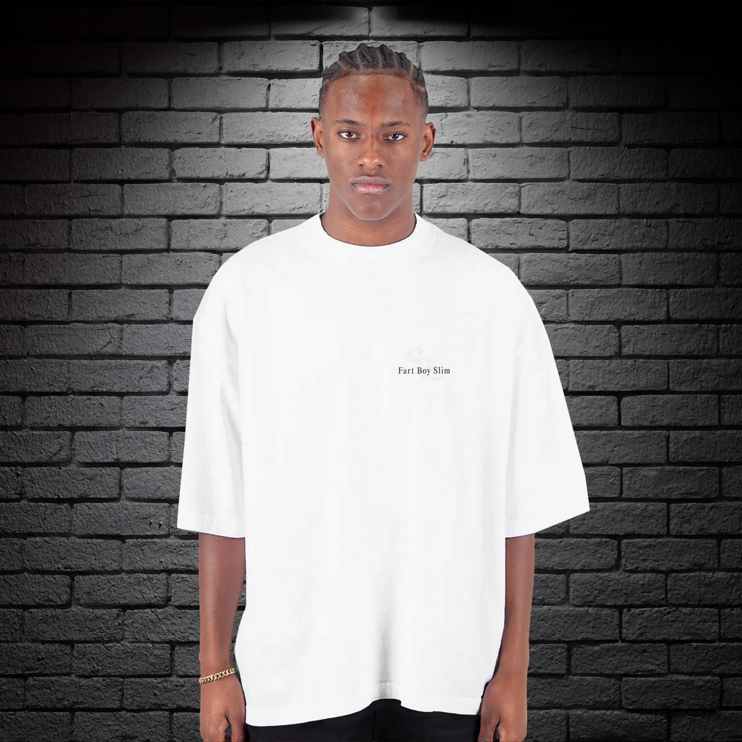 Front view of white oversized Fart Boy Slim t-shirt with subtle graphic, styled against a black brick wall.