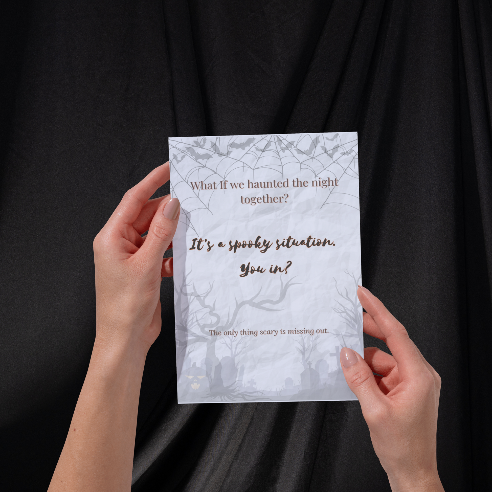Mockup of the What If Halloween Invite card held in two hands against a dark fabric background, showing the phrase “It’s a spooky situation. You in?” — perfect for casual fall gatherings.
