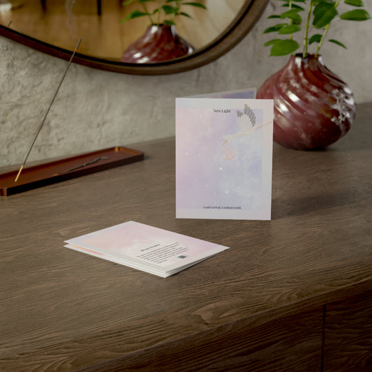 New Light baby card displayed on wooden dresser near incense holder and vase, featuring pastel artwork and soft lighting.
