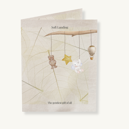 Soft Landing baby greeting card featuring a dreamy mobile with bear, bunny, star, and balloon, set on linen and leaf textures — a gentle welcome gift for new parents.

