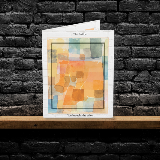 A folded A6 art greeting card titled “The Builder,” featuring an abstract watercolor design in warm orange, yellow, and soft blue tones. Displayed upright on a wooden shelf against a black brick wall. A minimalist greeting card perfect for Father’s Day, appreciation, or gifting to a stepdad or mentor.
